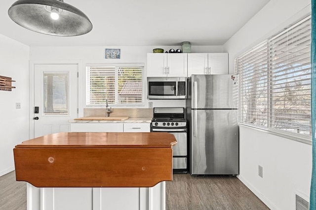 kitchen featuring baseboards, white cabinets, wood finished floors, a center island, and stainless steel appliances