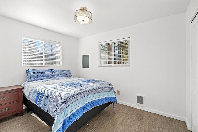 bedroom with electric panel, wood finished floors, visible vents, and baseboards