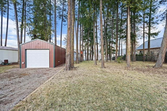 view of yard with driveway, a detached garage, fence, and an outbuilding