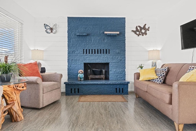 living room featuring a fireplace with raised hearth, wood walls, and wood finished floors