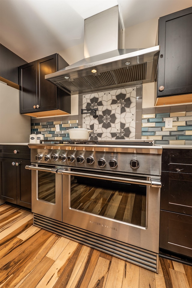 kitchen featuring wall chimney range hood, decorative backsplash, light wood-type flooring, and double oven range