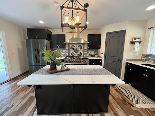 22410 S Ritchey Rd, Cheney, WA 99004 - kitchen with wall chimney exhaust hood, stainless steel appliances, dark cabinetry, tasteful backsplash, and light wood-type flooring