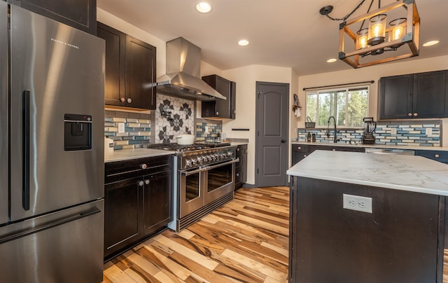 kitchen featuring wall chimney range hood, a sink, light wood-style flooring, stainless steel appliances, and recessed lighting