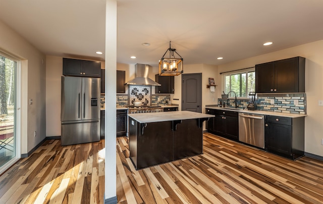kitchen featuring light countertops, appliances with stainless steel finishes, a sink, and wall chimney exhaust hood