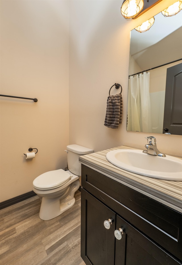 full bath featuring vanity, baseboards, wood finished floors, and toilet