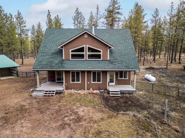 back of property with fence, covered porch, and a shingled roof