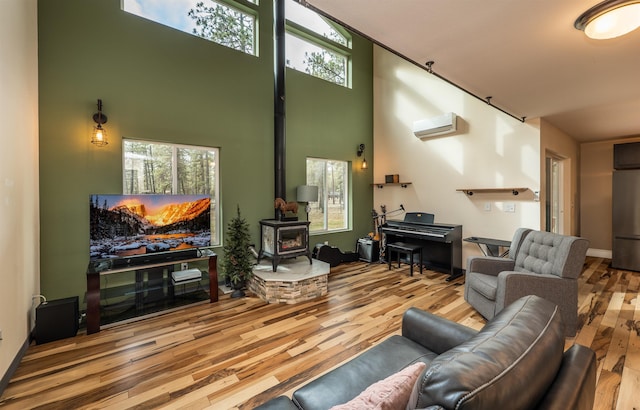 living area with a wall mounted AC, a wood stove, wood finished floors, and a towering ceiling