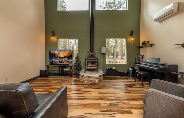 living room with a wall unit AC, a wood stove, wood finished floors, and a towering ceiling