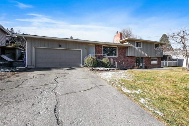 split level home featuring an attached garage, brick siding, driveway, a chimney, and a front yard