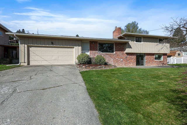 tri-level home featuring a chimney, driveway, an attached garage, a front yard, and brick siding