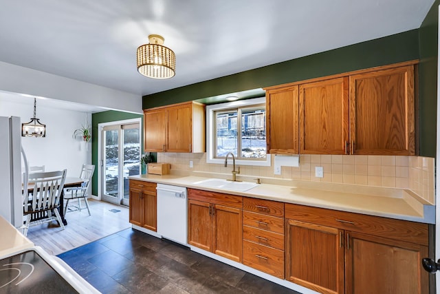 kitchen featuring a notable chandelier, white appliances, a sink, light countertops, and backsplash