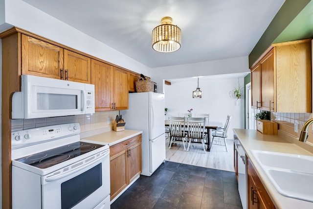 kitchen with a sink, decorative backsplash, white appliances, an inviting chandelier, and light countertops