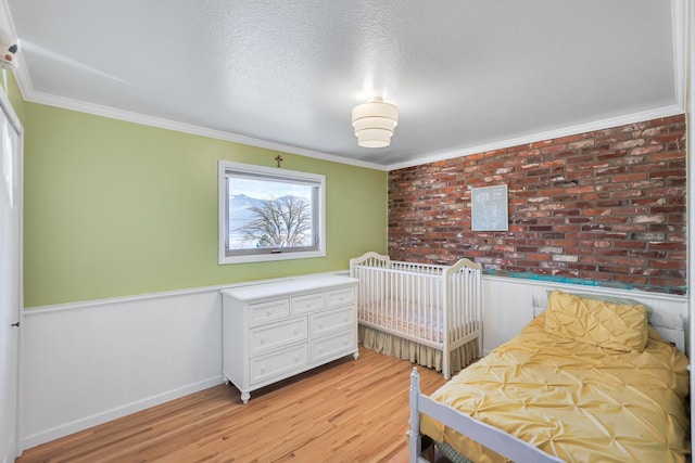 bedroom with a textured ceiling, light wood-type flooring, wainscoting, and crown molding