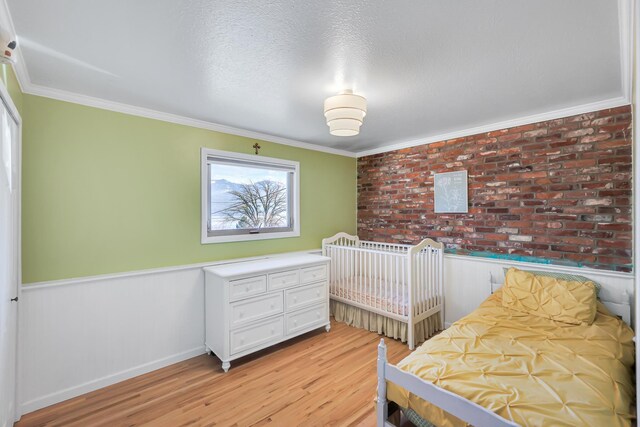 bedroom with light wood finished floors, a wainscoted wall, and ornamental molding