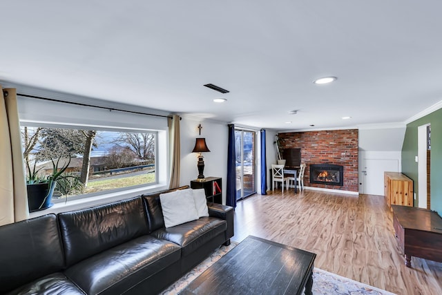 living room with recessed lighting, wood finished floors, visible vents, ornamental molding, and a brick fireplace