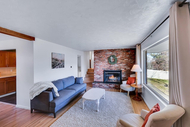 living room featuring baseboards, light wood-style flooring, beamed ceiling, a textured ceiling, and a fireplace