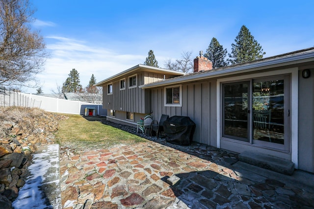 rear view of house with a lawn, a patio, a chimney, fence, and board and batten siding