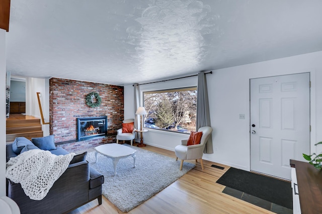 living area featuring a fireplace, light wood finished floors, visible vents, a textured ceiling, and baseboards