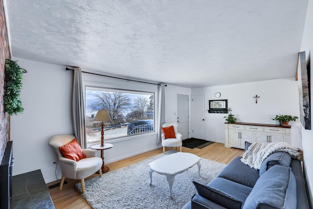 living area featuring a textured ceiling, light wood finished floors, and baseboards