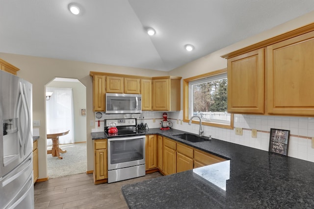 kitchen with arched walkways, lofted ceiling, backsplash, appliances with stainless steel finishes, and a sink