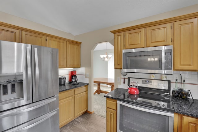 kitchen featuring arched walkways, a chandelier, stainless steel appliances, decorative backsplash, and dark stone countertops