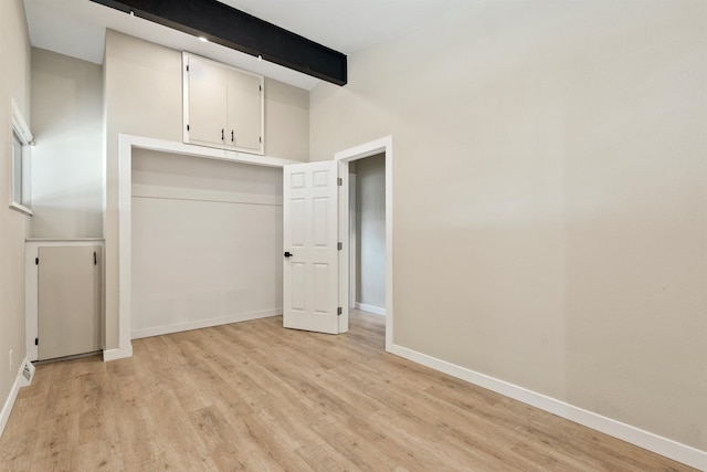 unfurnished bedroom with light wood finished floors, baseboards, and beam ceiling