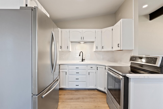 kitchen featuring light wood finished floors, decorative backsplash, lofted ceiling, appliances with stainless steel finishes, and white cabinetry