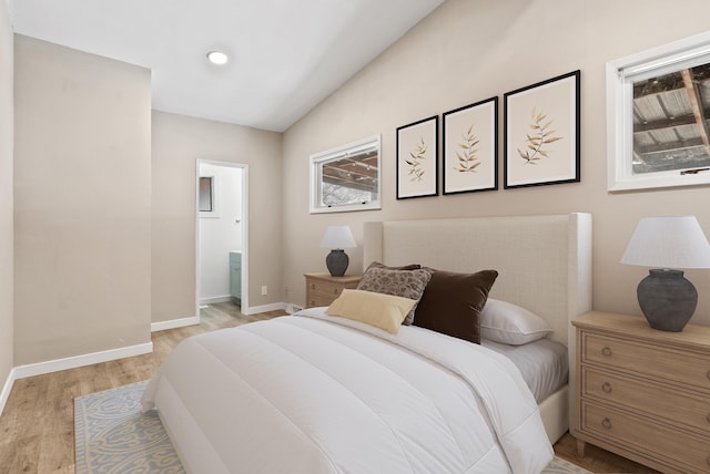 bedroom featuring baseboards, ensuite bathroom, vaulted ceiling, light wood-type flooring, and recessed lighting