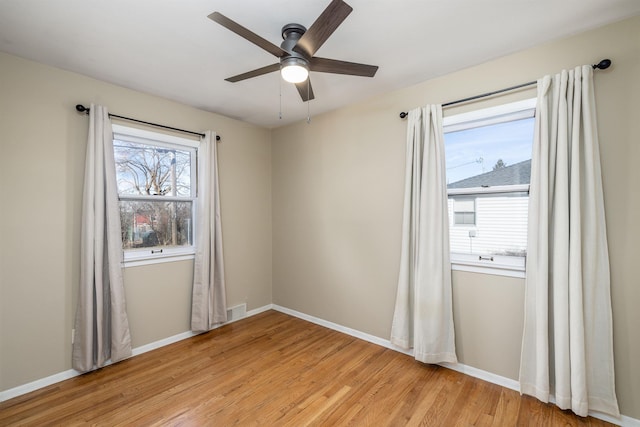 spare room featuring a ceiling fan, light wood-type flooring, visible vents, and baseboards