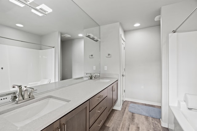 bathroom with recessed lighting, double vanity, a sink, and wood finished floors