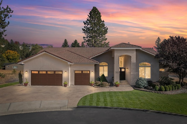 mediterranean / spanish-style house with a garage, a yard, a tiled roof, and stucco siding