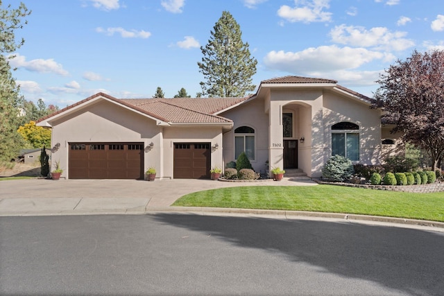 mediterranean / spanish-style home with stucco siding, concrete driveway, an attached garage, a front yard, and a tiled roof