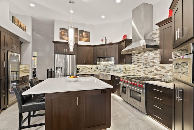 kitchen with dark brown cabinetry, decorative backsplash, wall chimney exhaust hood, high quality appliances, and a sink