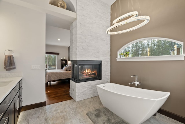 ensuite bathroom featuring a stone fireplace, vanity, baseboards, a soaking tub, and ensuite bath