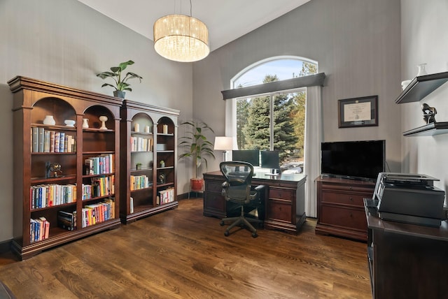 office with a towering ceiling, an inviting chandelier, baseboards, and dark wood-type flooring