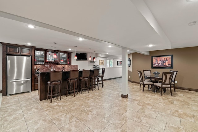 interior space with dark brown cabinets, freestanding refrigerator, tasteful backsplash, a kitchen bar, and glass insert cabinets