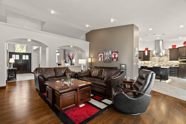 living room featuring lofted ceiling, arched walkways, wood finished floors, and recessed lighting