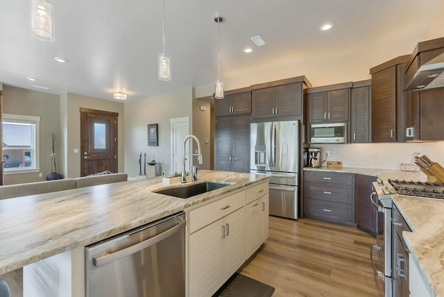 kitchen featuring decorative light fixtures, stainless steel appliances, tasteful backsplash, a sink, and light wood-type flooring