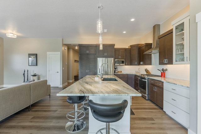 kitchen featuring light wood-style flooring, stainless steel appliances, a breakfast bar, a sink, and wall chimney exhaust hood