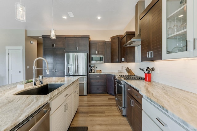 kitchen featuring appliances with stainless steel finishes, glass insert cabinets, a sink, dark brown cabinets, and wall chimney exhaust hood