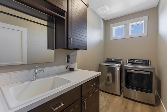 clothes washing area featuring light wood finished floors, cabinet space, visible vents, a sink, and separate washer and dryer