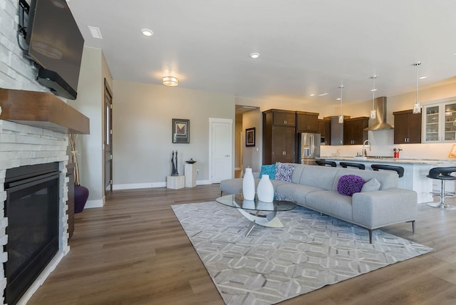 living area featuring light wood finished floors, a brick fireplace, recessed lighting, and baseboards