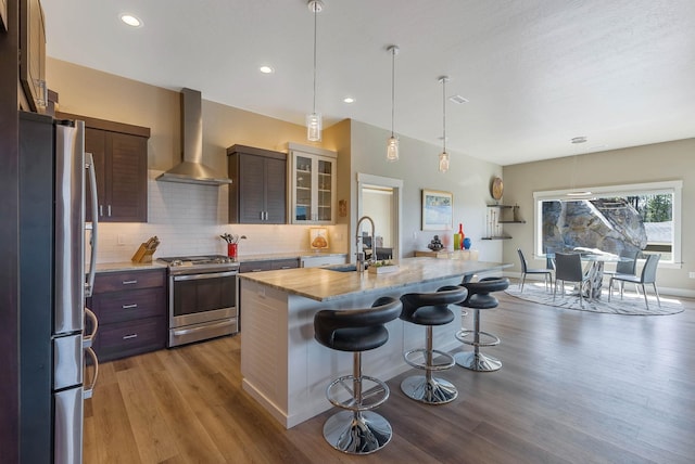 kitchen featuring wall chimney exhaust hood, a breakfast bar area, wood finished floors, stainless steel appliances, and a sink