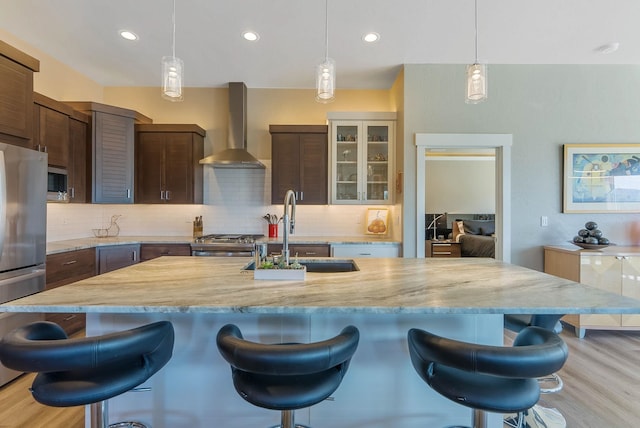 kitchen featuring wall chimney range hood, appliances with stainless steel finishes, a kitchen breakfast bar, and a sink