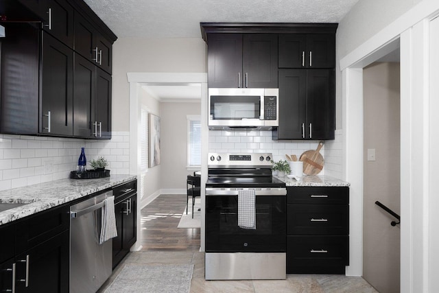 kitchen featuring stainless steel appliances, backsplash, light wood-style flooring, a textured ceiling, and light stone countertops