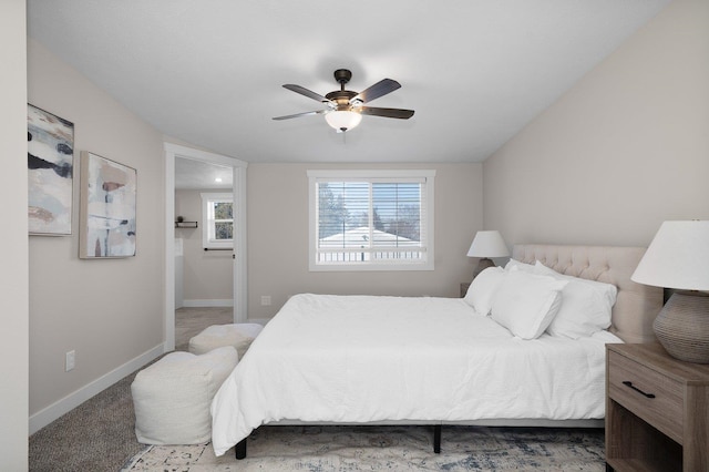 carpeted bedroom with ensuite bathroom, multiple windows, a ceiling fan, and baseboards