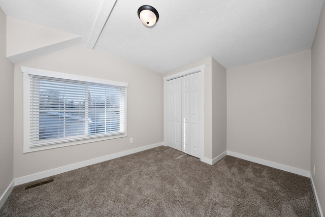 unfurnished bedroom featuring a closet, visible vents, dark carpet, vaulted ceiling, and baseboards