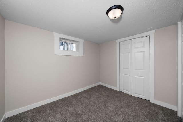 basement with a textured ceiling, dark colored carpet, and baseboards