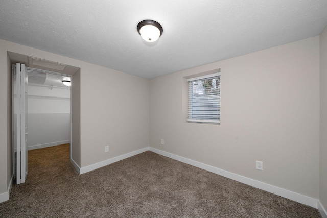 unfurnished bedroom with baseboards, a walk in closet, a textured ceiling, dark carpet, and a closet