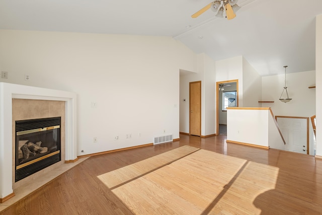 unfurnished living room with visible vents, a ceiling fan, wood finished floors, a tile fireplace, and baseboards